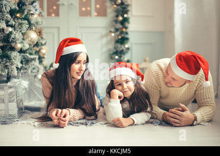 Famiglia nel natale cappelli di Babbo Natale giacente sul letto. madre padre e bambino divertirsi Foto Stock