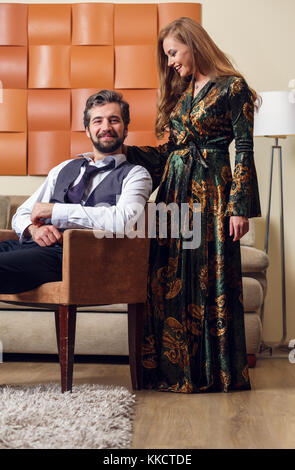 Immagine di uomo elegante su una sedia e dai lunghi capelli donna nel vestire Foto Stock