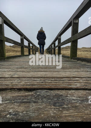 Una donna che cammina su un sentiero in st. peter-ording su un nuvoloso giorno di inverno Foto Stock