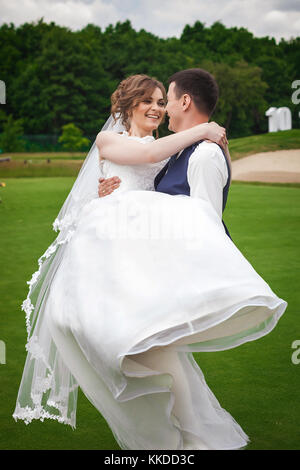 Lo sposo holding sposa su bracci, avvolgente e di girare intorno a lei nella natura Foto Stock