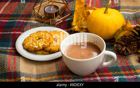 Caffè caldo o cioccolato in tazza calda coperta con i cookie e in autunno la zucca decorativa, coni e foglie secche, inverno concetto impostazione Foto Stock