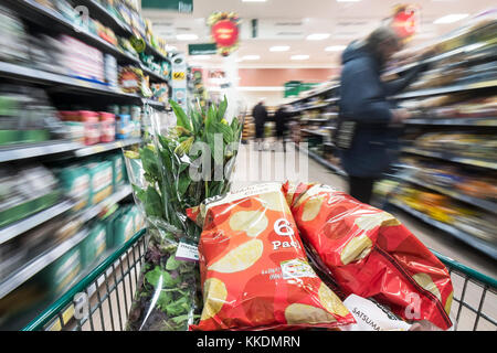 Un carrello della spesa pieno di merci sono spinti verso il basso un corridoio in un supermercato. Foto Stock