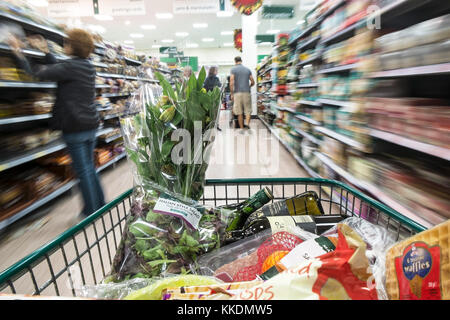 Un carrello della spesa pieno di merci sono spinti verso il basso un corridoio in un supermercato. Foto Stock