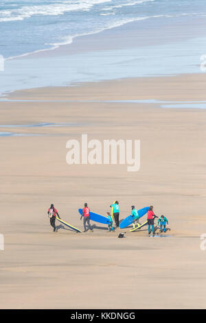 Surf - istruttori di una scuola di surf scuola di surf e giovani studenti a piedi al mare e il trasporto di tavole da surf a Fistral Beach Newquay Cornwal Foto Stock