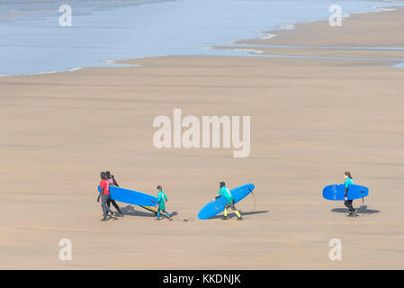 Surf - istruttori di una scuola di surf scuola di surf e giovani studenti a piedi al mare e il trasporto di tavole da surf a Fistral Beach Newquay Cornwal Foto Stock