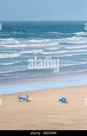 Surf - istruttori di una scuola di surf scuola di surf e giovani studenti a piedi al mare e trasportare le loro tavole da surf a Fistral Beach Newquay. Foto Stock