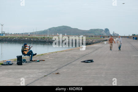 L'uomo musicista di strada su un Howth è pier a suonare e cantare canzoni romantiche per passare dai turisti. La penisola di Howth con Irlanda's Eye, Dublino, Irlanda Foto Stock