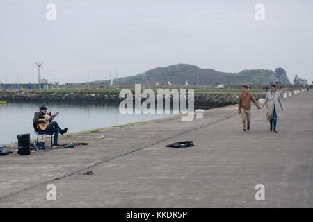 L'uomo musicista di strada su un Howth è pier a suonare e cantare canzoni romantiche per passare dai turisti. La penisola di Howth con Irlanda's Eye, Dublino, Irlanda Foto Stock