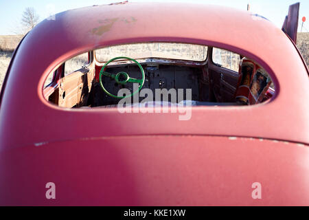 Retro del vetro rotto di un rosso vintage auto rottamata abbandonato all'aperto in un campo rurale in una vista ravvicinata Foto Stock