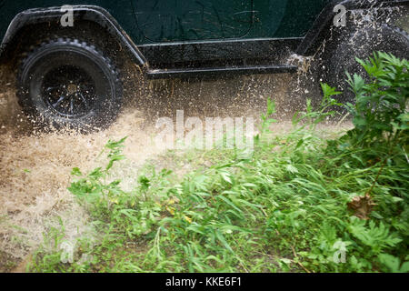 4wd guadato un flusso poco profonde a velocità provocando uno spruzzo di acqua dalle ruote in una stretta fino a basso angolo di visione Foto Stock