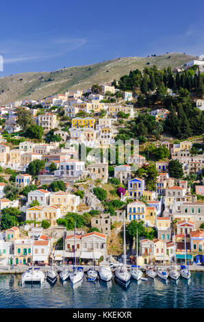 Barche ormeggiate lungo il panoramico lungomare di Yialos città sull'isola di Symi, Grecia Foto Stock