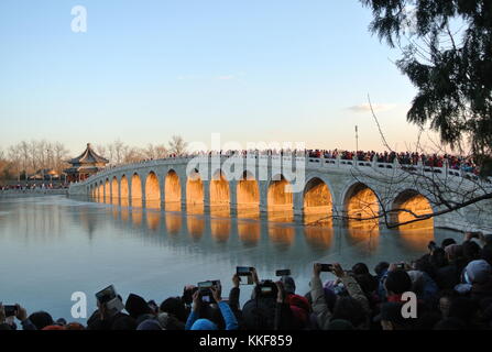Pechino, Cina. 6 dicembre 2017. I visitatori ammirano il paesaggio del crepuscolo che splende attraverso il ponte del diciassettesimo arco nel Palazzo d'Estate di Pechino, capitale della Cina, il 6 dicembre 2017. Credito: Ma Zhihong/Xinhua/Alamy Live News Foto Stock