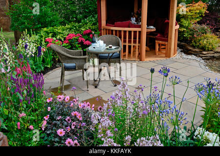 Il patio in un giardino acquatico con fiori colorati in frontiera e posti a sedere attraente Foto Stock