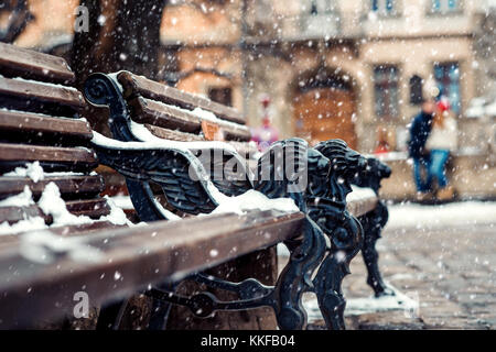 Vista ravvicinata della panca con ferro decorazioni lions ricoperta di neve soffice. abbracciando il paio con il cane a sfondo sfocato. Foto Stock