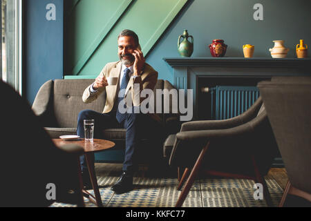 Vista l'età media di imprenditore a bere caffè e utilizzando il telefono cellulare nella lobby Foto Stock