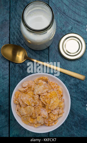 Corn flakes in una ciotola con cucchiaio e bottiglia di latte. Foto Stock