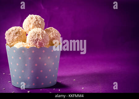 Praline di cocco nel bicchiere su sfondo viola,fuoco selettivo e uno spazio vuoto Foto Stock