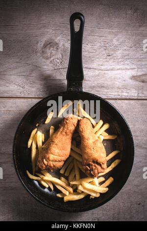 Le patatine fritte e le cosce di pollo nella padella dal di sopra Foto Stock