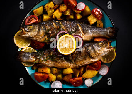 Bass grigliate di pesce e patate al forno nella piastra,fuoco selettivo Foto Stock