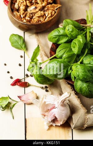 Mazzetto di basilico fresco, tazza di noci, pepe e aglio servita su bianco tavolo in legno. Vedere serie Foto Stock
