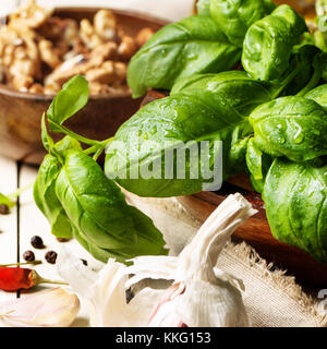 Mazzetto di basilico fresco, tazza di noci, pepe e aglio servita su bianco tavolo in legno. Vedere serie Foto Stock