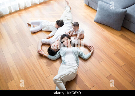 Felice giovane famiglia cinese in appoggio su pavimento in legno Foto Stock