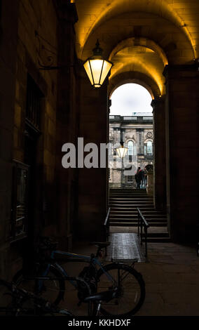 Edimburgo, Scozia, Regno Unito. 1 dicembre, 2017. Uno studente in abito di graduazione nel vecchio cortile College, South Bridge, Università di Edimburgo, con vecchio stile vittoriano lampade accese nel buio pomeriggio nel corridoio esterno Foto Stock