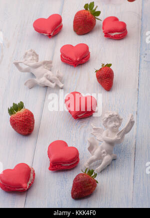 I cookie di colore rosso a forma di cuore le fragole e decorate con angelo su assi di legno il giorno di san valentino Foto Stock