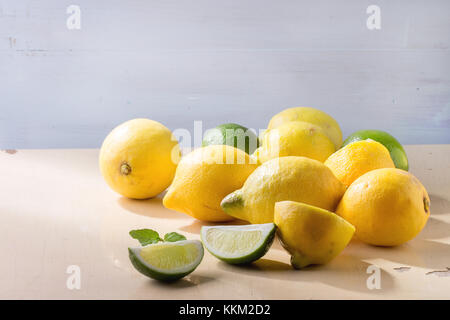 Cumulo di tutto e fette di limoni e limette oltre il bianco sullo sfondo di legno. rustica della luce del sole. Foto Stock