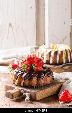 In casa torte al cioccolato con fragole e cioccolato fondente ganache e glassa bianca e la scorza di limone e servite su piccole in legno schede di taglio su w Foto Stock