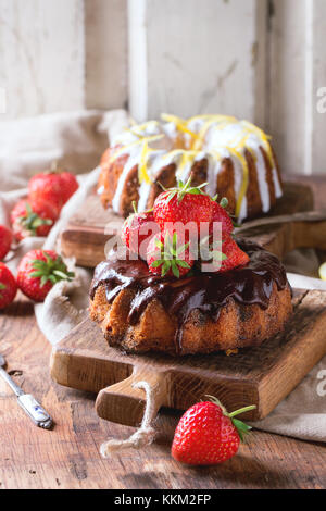 In casa torte al cioccolato con fragole e cioccolato fondente ganache e glassa bianca e la scorza di limone e servite su piccole in legno schede di taglio su w Foto Stock