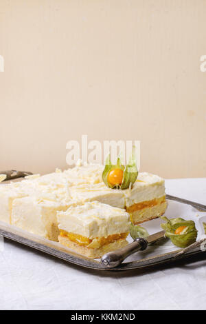 In casa fette di torta con mousse cremosa e frutti tropicali di mango e physalis servita nel vintage vassoio di metallo su tavolo bianco Foto Stock