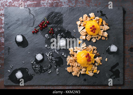 Mango sorbetto gelato, servita su wafer briciole con ribes rosso e bacche di cubetti di ghiaccio sopra nero ardesia. vecchio sfondo metallico. vista dall'alto. Foto Stock