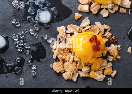 Mango sorbetto gelato, servita su wafer briciole con ribes rosso e bacche di cubetti di ghiaccio sopra nero ardesia. vista dall'alto. Foto Stock