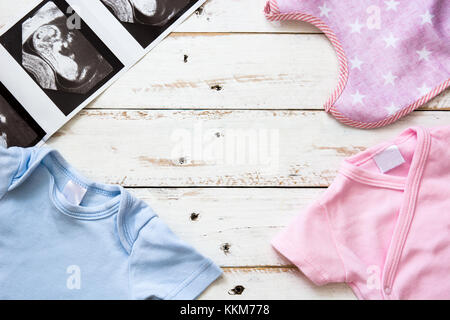 Rosa e azzurro baby romper e ultrasuoni in bianco sullo sfondo di legno.copyspace Foto Stock