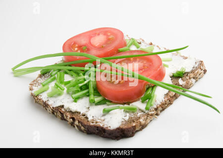 Basso angolo di visione su una fetta di pane con la crema di formaggio, due fette di pomodoro ed erba cipollina su sfondo bianco. Foto Stock