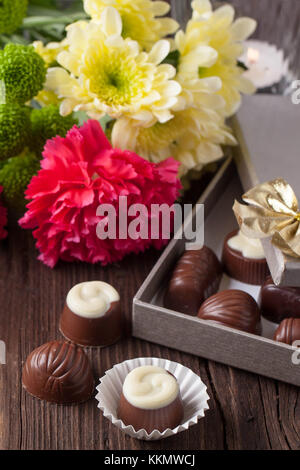 Cioccolatini, fulmine candela e mazzo di fiori di garofano e crisantemo fiori sul vecchio tavolo in legno Foto Stock