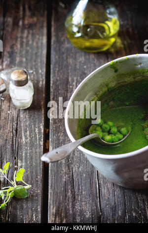 Minestra di crema di piselli verdi in coppa in alluminio con cucchiaio vintage riempire intere piselli. sopra il vecchio tavolo in legno. scuro in stile rustico, la luce naturale del giorno. Foto Stock