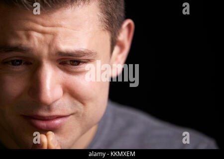 Close up di pianto bianco giovane uomo che guarda verso il basso, orizzontale Foto Stock