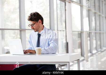 Giovane imprenditore ad una scrivania di lavoro sul suo computer portatile Foto Stock