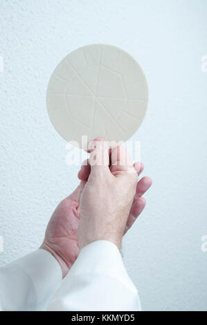 Un sacerdoti mani detiene l'host pane consacrato nell Eucaristia. Parte di una Chiesa comunione religiosa cerimonia o un servizio. Foto Stock