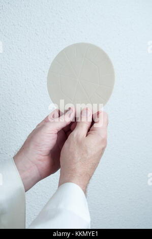 Un sacerdoti mani detiene l'host pane consacrato nell Eucaristia. Parte di una Chiesa comunione religiosa cerimonia o un servizio. Foto Stock