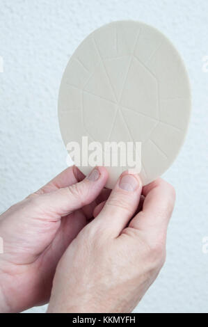 Un sacerdoti mani detiene l'host pane consacrato nell Eucaristia. Parte di una Chiesa comunione religiosa cerimonia o un servizio. Foto Stock