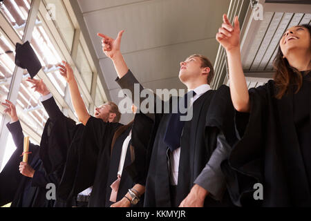 I laureati in abiti gettando le loro schede di mortaio in aria Foto Stock
