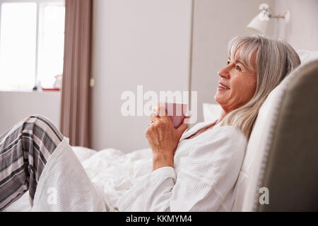 Senior donna relax nel letto con bevanda calda Foto Stock