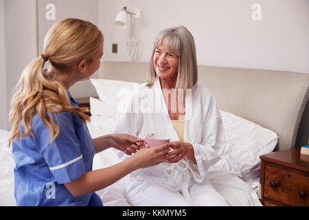 L'infermiera facendo visita a casa Senior donna nel letto Foto Stock