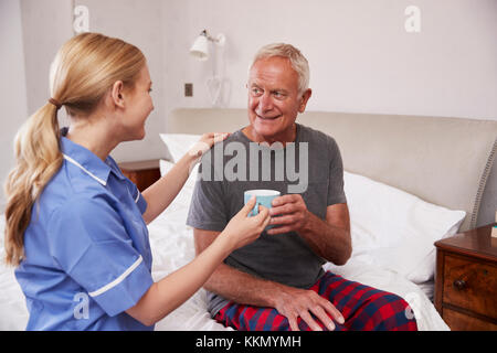 L'infermiera facendo visita a casa Senior uomo nel letto Foto Stock