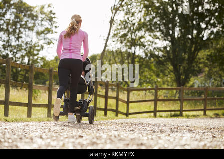 Vista posteriore della madre esercita eseguendo e spingendo Baby Buggy Foto Stock