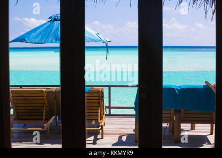 Vista dall'interno del bungalow attraverso la finestra nelle Maldive. Sul ponte ci sono sedie a sdraio e ombrellone. Si tratta di una splendida vista Foto Stock