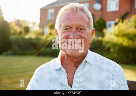 Senior uomo seduto sulla panchina da giardino in sera la luce solare Foto Stock